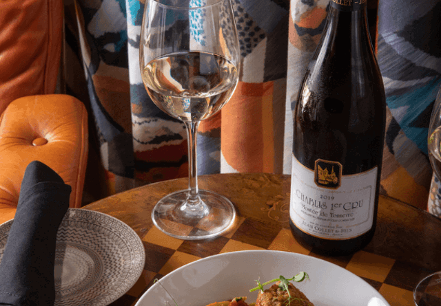 A bottle of wine paired with a plate of gourmet food, featuring artful presentation and a warm, inviting dining setup.