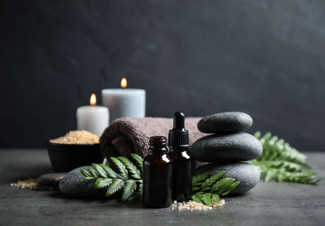 Serene layout with lit candles, hot stones, massage oil and towel. 