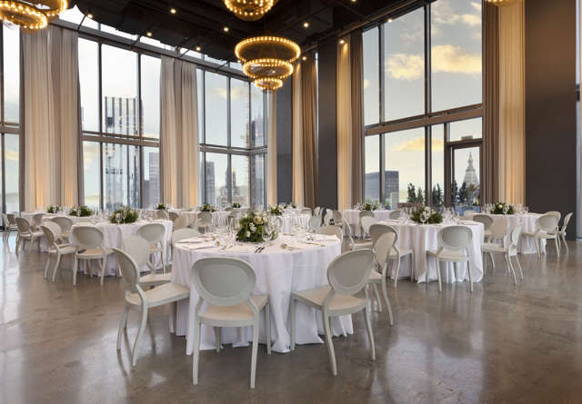 Elegant event space with round tables, white linens, and stunning city views through large windows.