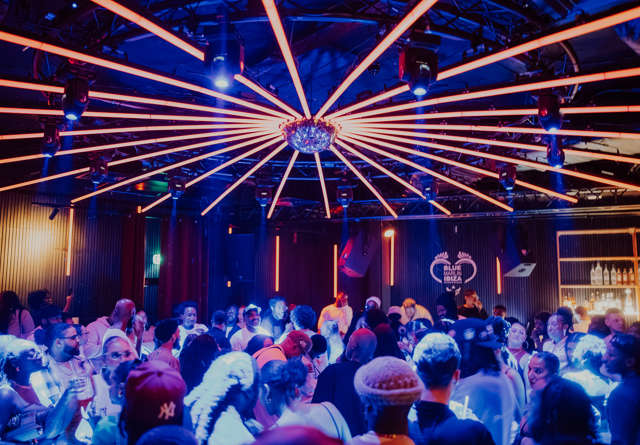 A nightclub scene with a vibrant crowd dancing under neon orange lights radiating from a central chandelier.