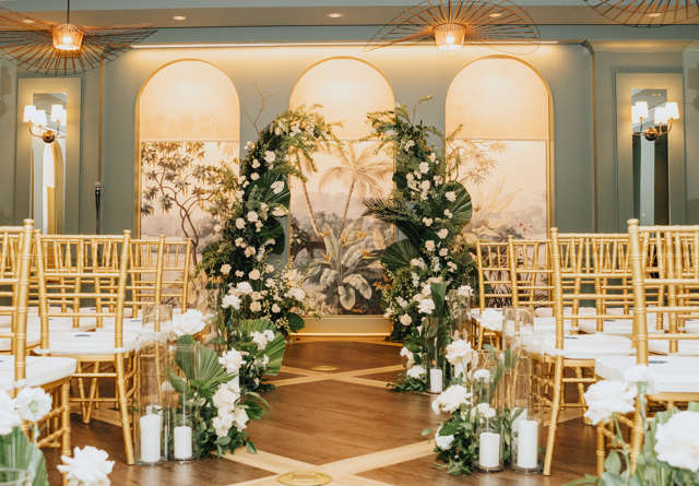 Wedding ceremony inside Virgin Hotels New Orleans setup with white chairs, floral arrangements, and a beautiful backdrop.